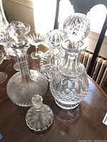 Photo showing four glass decanters on wooden table with window light