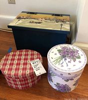 Photo showing rectangular blue wooden decorative box with winter scene painting on lid, and two round nesting boxes with floral and checkered designs placed on floor.
