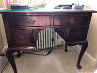 Front view of vintage desk showing wood finish, five drawers with metal handles, curved legs, and carved detailing.