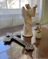 Metal wall cross with embossed crucifix, showing front view on table near window light.