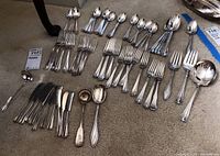 Full lot of Rogers Bros. silver flatware laid out on carpeted floor including forks, knives, spoons, serving spoons, and ladles.