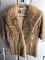 Front view of vintage beige mink fur stole hung on a hanger showing the soft fur texture and label inside.