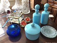 Overview of all glass and decorative items including blue glass bottles, paperweights, bowl, covered dish, decorative dish, glass rose, and mirrored box.