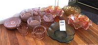 Overview of the glassware collection showing pink depression glass items alongside iridescent orange carnival glass pieces and a green depression glass bowl.