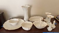Photo showing collection of Lenox white porcelain serving pieces including the tall vase, bowl, handled dish, chip and dip plate, candle holders, salt and pepper shakers, and other plates, all with textured floral and leaf patterns.