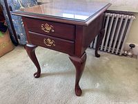 Side view of the night stand showing two drawers with brass handles and a glass top.
