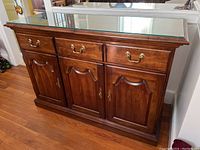Front view of the Jamestown Sterling wooden server with glass top showing 3 drawers and 3 cabinets closed.