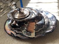 Overhead photo of silver plated serveware including trays and lid with handle, showing tarnish and wear.