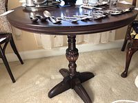 Full view of the round wooden side table with carved pedestal base and four feet, showing the dark wood finish and polished surface.