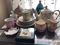View of the full lot with various teapots, cups, plates, and decorative containers arranged on a table.