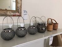 Photo of six votive candle holders on a shelf including five identical textured glass holders with metal handles and one holder with larger stud texture.