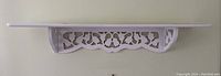 Front view showing full length of white wooden wall shelf with detailed carved lower bracket.