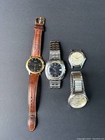 Four men's vintage wristwatches laid out on a black surface, showing different styles and straps.