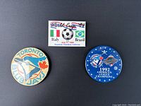 Three vintage buttons placed on black background: one beige Toronto Blue Jays, one blue 1992 Blue Jays Champion, one rectangular 1994 World Cup button.