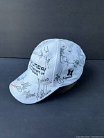 Front-left angle view of white golf cap showing Hyundai and Kapaska logos and multiple autographs on front and side panels.