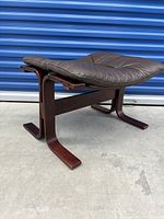 Side angled view of vintage foot stool showing curved wood legs and padded leather top.
