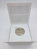 View of the medal inside the white box with descriptive text on the inside lid about the design inspiration and Olympic motto in English and French.