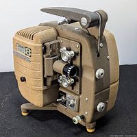 Sekonic 8mm film projector side view showing lens, controls, and feet on black surface