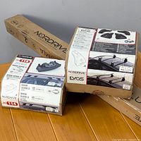Two unopened original Nordrive boxes: Kit 114 for BMW Series 3 with 2 aluminum cross bars and feet; Evos support feet. Labeling and packaging clearly visible.