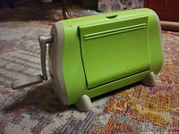Angle view of the green Cuttlebug machine with crank handle on a carpet.