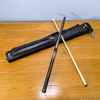 Pool cue laid across hard carrying case on wood floor