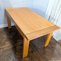 Full view of rectangular oak wood dining table showing natural grain and sturdy legs on dark herringbone wood floor.
