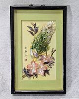 Framed rectangular artwork showing a peacock with detailed stone feather inlays and flowers set on pale background with calligraphy. Framed in a black lacquered frame with glass.