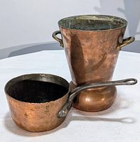 Photo showing both copper items side by side on a white surface under natural light. Visible patina and rivets on both pieces.
