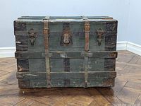 Front and angled view of the old steamer trunk showing original leather straps, wood slats, and metal locking mechanisms on a hardwood floor.