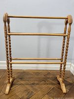 Front view of the antique wooden quilt rack showing three horizontal bars and turned spindle vertical supports.