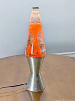 Front view of the vintage lava lamp showing orange wax lava inside clear liquid and brushed metal base with minor wear.
