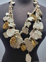 Front view of the multi-strand necklace showing large white magnesite stones with brown veining and teardrop-shaped pyrite pendants on a black mannequin.