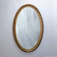 Full view of the vintage oval mirror with gold ornate frame hanging on a white wall.