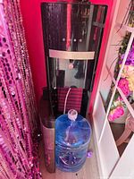 Photo showing a black and stainless steel water cooler dispenser next to a 5 gallon refillable blue water tank bottle with white cap.