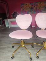 Front view of one pink heart-shaped rolling chair showing plush upholstered seat and heart-shaped back, on gold metal base with casters.
