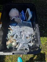 View into large bin revealing various Christmas decorations including star ornaments, snowflakes, pine branches, baubles, and stuffed holiday figure.
