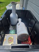 Two white ceramic bottles labeled 'Chateau Fontaine' placed inside a black plastic bin with the six assorted vintage cigar boxes at the bottom.