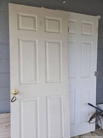 Photo showing two white paneled interior doors leaning against a wall, both with brass-colored knobs attached.