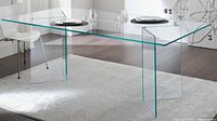 Photo shows thick clear glass table with glass legs in room setting, set for two dining or work stations.