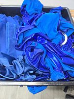 Bin containing multiple blue cloth napkins and chair sashes in varying shades of blue and textures.