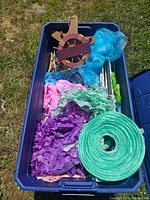 Overhead view of filled blue plastic bin showing various colorful seaside themed decoration items including crepe paper, nets, wooden signage, and artificial coral.