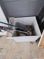 Photo of the white utility sink with attached drainboard filled with miscellaneous tools and parts, placed indoors against a gray concrete block wall.