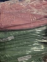 Two large pieces of round satin table linen in pink and green, wrapped in plastic with labels visible on each.