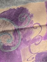 Close-up photo of fabric showing purple and beige colors with teal swirl print, one of the printed tablecloths in the lot.
