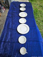 Multiple white plates arranged on blue cloth showing size gradation and single teacup at the end
