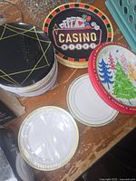 Various round serving trays with decorative prints and disposable plates stacked on wooden surface