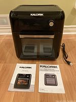 Front view of closed Kalorik smart fryer oven with power cord and two user manuals laid out in front.