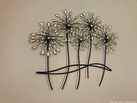 Front view of metal wall art showing five stylized flowers with black stems and silver teardrop petals attached to a wave-like black metal base.
