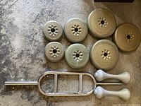 Photo showing assorted weight plates and short barbell with two white dumbbells on concrete floor