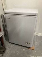 Closed Danby DCF401 chest freezer showing front and side, white color, sitting on floor with wooden support at base.